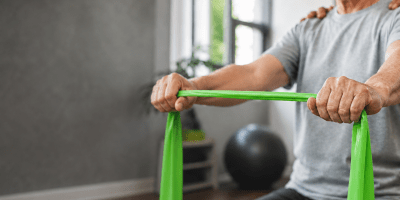 Older adult using a green resistance band during physical therapy.